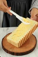 Female Hand Spreading Butter on Roti Bakar Bandung Bread using White Spatula. photo