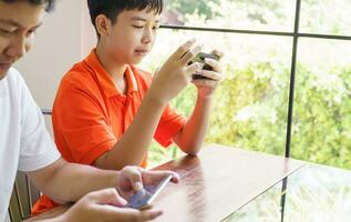 asiático padre y hijo con móvil teléfono jugando juegos juntos papá gastar hora con niños familia. foto