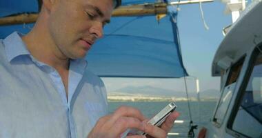 Man is typing on his smartphone while he sails on the boat in summer sunny day video