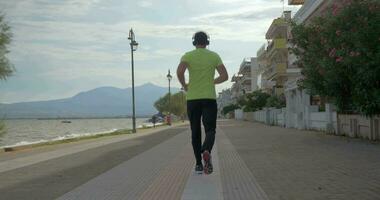 joven hombre en auriculares carreras en la carretera de ciudad perea, Grecia video