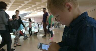 enfant en utilisant intelligent téléphone dans occupé achats centre video