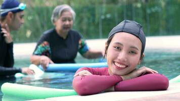 retrato de joven entrenador mujer en agua en frente de mayor mujer aeróbicos y trabajando fuera en el piscina. antiguo mujer haciendo agua aeróbicos ejercicio en el nadando piscina, mayor Deportes video