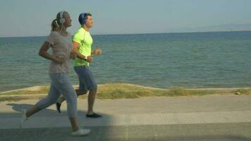 Man and woman running on pavement next to the sea video