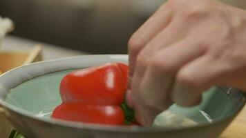 professioneel chef bereidt zich voor en bezuinigingen rood klok peper. dichtbij omhoog langzaam beweging video