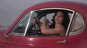 Young spectacular woman with long black hair and bright makeup sitting inside a red vintage car. Slow Motion video