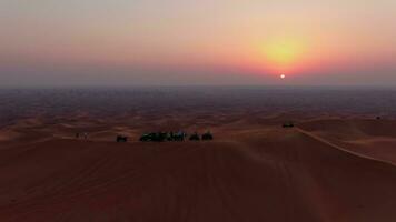 A drone flies over ATVs standing on the sand dunes of the desert against the backdrop of the sunset. Aerial view video