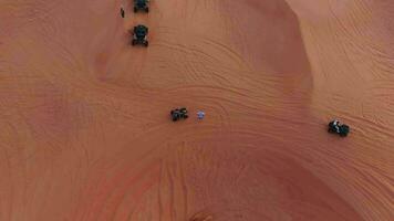 A drone flies over quad bikes driving through the sand dunes of the desert in the United Arab Emirates. Aerial view video