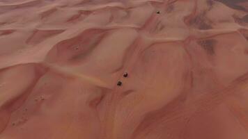 A drone flies over quad bikes driving through the sand dunes of the desert in the United Arab Emirates. Aerial view video