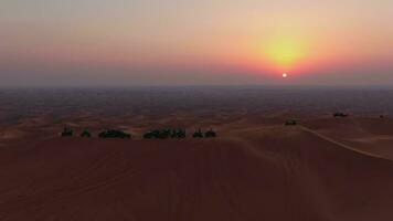 A drone flies over ATVs standing on the sand dunes of the desert against the backdrop of the sunset. Aerial view video