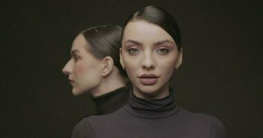 deux Jeune élégant femmes avec bien maquillage sur une noir Contexte. lent mouvement, studio tir. video