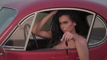 Young spectacular woman with long black hair and bright makeup sitting inside a red vintage car. Slow Motion video