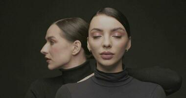 dos joven elegante mujer con bueno maquillaje en un negro antecedentes. lento movimiento, estudio disparo. video