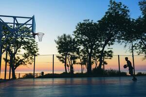 black man doing sports, playing basketball on sunrise, silhouette photo