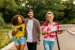 happy young company of smiling friends walking in park with electric kick scooter photo