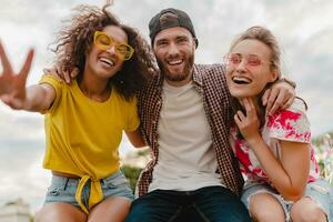 happy young company of smiling friends sitting in park photo