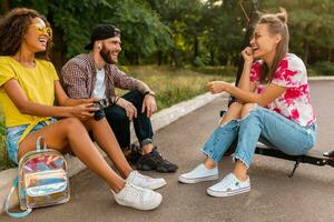 contento joven empresa de sonriente amigos sentado en parque en césped con eléctrico patada scooter foto