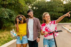 contento joven empresa de sonriente amigos caminando en parque con eléctrico patada scooter foto