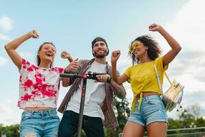 happy young company of smiling friends dancing walking in street with electric kick scooter photo