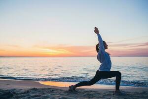 young woman doing sport exercises on sunrise beach in morning photo