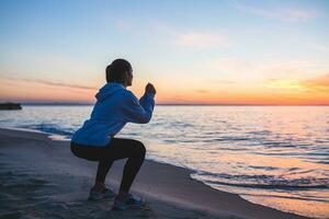 young woman doing sport exercises on sunrise beach in morning photo