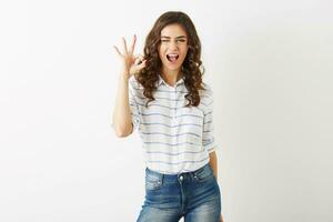 portrait of young attractive woman with exited face expression showing positive gesture, smiling, happy, winking, hipster style, isolated, curly hair, okay sign, cheerful mood, beautiful face photo