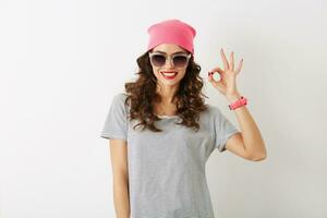 retrato de joven bonito mujer demostración bueno firmar, en rosado sombrero, Gafas de sol, sonriente, aislado foto