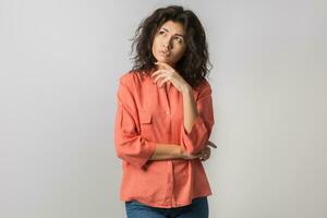 retrato de joven pensativo morena mujer en naranja camisa, Rizado cabello, verano estilo, frustrado cara expresión, mirando arriba, pensamiento, problema, idea, mezclado carrera, aislado foto