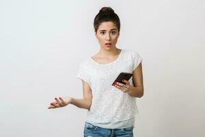 shocked young woman holding smart phone, opened mouth, looking into camera, surprised face expression, isolated on white background, having a problem photo