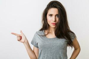 atractivo joven mujer en gris camiseta señalando dedo, aislado en blanco estudio fondo, gesticulando foto