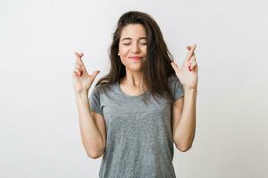 young pretty woman making a wish crossed her fingers, luck, closed eyes, hopeful gesture, isolated on white studio background photo