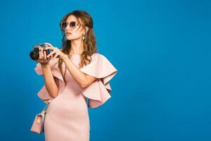 young stylish sexy woman in pink luxury dress taking pictures on vintage camera photo