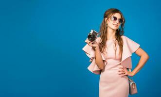 young stylish sexy woman in pink luxury dress taking pictures on vintage camera photo