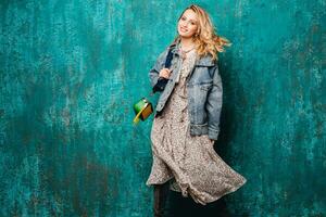 attractive stylish blonde woman in jeans oversize jacket walking against wall fashion photo