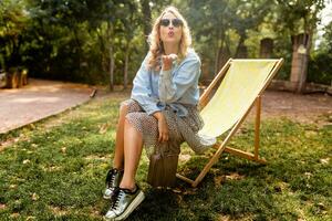 stylish blond woman sitting in city park summer fashion photo