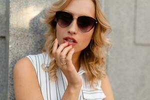 close-up portrait of young attractive stylish blonde woman in city street in summer fashion style photo