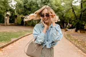 attractive blond smiling woman walking in park in stylish outfit photo