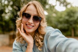 attractive blond smiling woman walking in park in stylish outfit photo