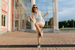 young attractive stylish woman running jumping funny in sneakers in city street photo