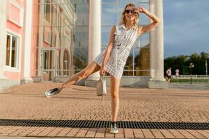 young attractive stylish woman running jumping funny in sneakers in city street photo