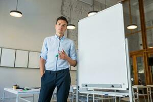 confident young handsome smiling man standing at empty white board with marker photo