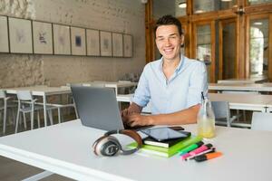 happy young confident man working on laptop, sitting in co-working office photo