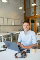 young handsome smiling man sitting in open space office working on laptop photo