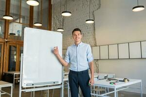 young handsome smiling man standing at empty white board with marker photo