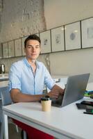 contento joven confidente hombre trabajando en computadora portátil, sentado en trabajo colaborativo oficina foto