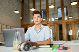 happy young confident man working on laptop, sitting in co-working office photo
