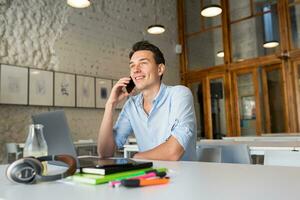 happy young confident man working on laptop, sitting in co-working office photo