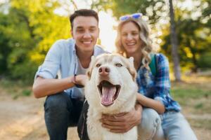 funny young stylish couple playing with dog in park photo