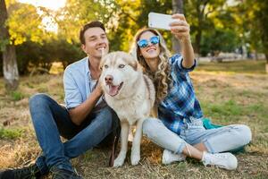 funny young stylish couple playing with dog in park photo