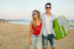 young smiling couple having fun on beach walking with surf board photo