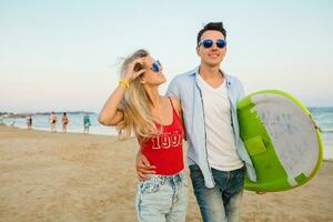 young smiling couple having fun on beach walking with surf board photo